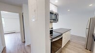 Located at 535-555 Shaw Ave in Coquitlam, BC, this one-bedroom, one-bathroom unit offers a well-organized, single-level layout designed for comfortable everyday living. The open-concept kitchen and living area forms the heart of the home, featuring light wood laminate flooring that runs throughout. The kitchen is outfitted with crisp white cabinetry, a white subway tile backsplash, dark countertops, stainless steel appliances including a full-size refrigerator and dishwasher, and a peninsula with additional counter space — ideal for casual dining or meal prep. Recessed lighting brightens the kitchen, while the adjacent living area benefits from a large sliding glass door that opens onto a private balcony overlooking mature greenery, filling the space with natural light. The bedroom is a comfortable size with a window offering views of the surrounding neighbourhood and baseboard heating for year-round warmth. A dedicated closet provides ample storage. The bathroom is clean and functional, finished with white subway tile surround in the tub area, light tile flooring, a frosted glass door, and chrome fixtures. Throughout the unit, white walls and light flooring contribute to a bright, neutral aesthetic that is easy to personalize.