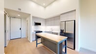 This thoughtfully designed 2-bedroom, 1-bathroom residence offers a clean, modern aesthetic with light hardwood flooring and crisp white walls throughout its single-floor layout. The standout kitchen features soaring ceilings, sleek gray shaker-style cabinetry extending to the ceiling, a herringbone tile backsplash, and a full suite of stainless steel appliances including a gas range, built-in microwave, dishwasher, and French door refrigerator. A butcher block-topped island with open lower shelving provides additional workspace and storage. The open living area adjoins the kitchen and benefits from natural light streaming through a large window framing outdoor greenery. Both bedrooms are bright and airy, with the primary bedroom offering a generous walk-in closet with full-perimeter hanging rods. A second walk-in closet serves the additional bedroom. The shared bathroom is finished with a wide vanity, clean white countertops, and a separate water closet, with in-unit laundry conveniently located nearby. A ductless mini-split system ensures year-round climate comfort. The hallway efficiently connects all rooms, making for a practical and well-organized floor plan.
