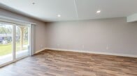Located at 123 Alexandra Drive in Laconia, NH, this thoughtfully designed multi-level home offers 2 bedrooms, 2 bathrooms, and three distinct floors of living space. The main level features a standout kitchen appointed with slate-blue shaker cabinetry, a white quartz waterfall peninsula, subway tile backsplash, stainless steel appliances, and warm hardwood flooring. Pendant lighting above the peninsula adds a refined touch, while the open layout connects seamlessly to the adjacent living area. A private deck off this level offers serene, tree-lined views of the surrounding landscape. The upper level hosts two comfortable carpeted bedrooms, including a spacious primary suite with a walk-in closet. A ceiling fan and natural light from a large window enhance the secondary bedroom. Both bathrooms are finished with neutral tile flooring, gray vanities, and matte black fixtures — one featuring a full tub/shower combination. The lower level provides an additional living area with luxury vinyl plank flooring, recessed lighting, a wall-mounted mini-split HVAC unit, and its own access point, offering flexibility for various uses. Hallways and staircases connect all three levels efficiently, creating a cohesive and functional flow throughout the home.