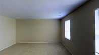 This single-story space presents a straightforward and functional interior layout. The room visible in the image is finished with wall-to-wall carpeting in a neutral beige tone, providing a soft and comfortable underfoot feel. The walls are painted in a warm taupe hue, lending a subdued, neutral ambiance that offers versatility for a range of uses and furnishing styles.

The ceiling is smooth and white, featuring a centrally placed HVAC vent, indicating a climate-controlled environment. A window fitted with horizontal blinds is positioned along one wall, allowing natural light to filter into the space while maintaining privacy. The natural light entering through the blinds contributes to a bright and airy atmosphere within the room.

White baseboards run along the perimeter of the room, providing a clean contrast against the taupe walls and beige carpet. The overall design is minimalist and move-in ready, offering a blank canvas that can easily be adapted to suit personal preferences. The single-floor layout ensures easy accessibility and straightforward navigation throughout the space.