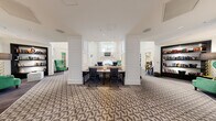 Located at 750 Thornton Way in Alexandria, Virginia, this sophisticated single-floor clubhouse showcases a refined blend of classic architectural details and bold contemporary design. The grand entry foyer sets a distinguished tone with an intricate parquet wood floor inlaid with contrasting geometric borders, flanked by stately white columns and anchored by a striking navy drum pendant light overhead.

The expansive main lounge features soaring ceilings adorned with sculptural gold geometric pendant fixtures, crisp white wainscoting panels, and plush patterned carpeting throughout. A statement marble fireplace serves as the room's focal point, framed by elegant millwork and topped with a mounted television, while tufted accent chairs in contrasting tones invite relaxed seating nearby.

A dedicated conference or meeting area offers a central work table surrounded by black chairs, set within a paneled alcove framed by tall architectural columns. Adjacent, a vibrant library lounge draws the eye with deep emerald-green walls, dark built-in shelving displaying curated artwork, a tufted teal velvet sofa, and cognac leather armchairs atop a bold black-and-white geometric rug.

The formal dining room continues the emerald palette with vivid green walls, a dramatic black-and-gold pendant light, and a round dark-lacquered dining table surrounded by tall upholstered ivory chairs. Throughout, gold accents, art glass panels, and layered textiles unify the space with a cohesive, upscale aesthetic.