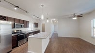 This single-floor residence offers a thoughtfully designed open-concept layout that seamlessly connects the kitchen, dining, and living areas. The kitchen is a standout feature, equipped with rich dark espresso cabinetry, granite countertops, a large central island, stainless steel appliances including a refrigerator, range, microwave, and dishwasher, and a double-basin sink beneath a bright window. Track lighting overhead provides ample task illumination, while pendant lights add a refined touch above the island. A built-in wine rack adds a functional yet stylish accent. The expansive living area is finished with warm hardwood-style flooring and features a ceiling fan with light fixture, along with multiple windows dressed in blinds that invite natural light while maintaining privacy. The bedroom continues the clean, neutral palette with plush carpeting, dual windows, and a ceiling fan for comfort. The bathroom is generously proportioned, featuring a long dual-sink vanity with dark cabinetry and ample counter space, a soaking tub with tile surround, and wood-style flooring. Throughout the space, crisp white walls, consistent trim, and a cohesive design language create a modern, move-in-ready environment that is both functional and inviting.