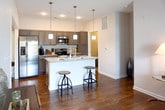 Located at 712 Promenade Place in Virginia Beach, Virginia, this single-floor residence offers a well-designed layout with contemporary finishes throughout. The kitchen is a standout feature, showcasing gray shaker-style cabinetry, granite countertops, a mosaic tile backsplash, stainless steel appliances, and a large island with bar seating and pendant lighting overhead — ideal for both cooking and casual dining. Wood-style flooring runs through the main living areas, adding warmth and visual continuity. The living room is bright and inviting, centered around a sliding glass door that opens to a private balcony with outdoor views. Multiple bedrooms are carpeted for comfort; one features dual windows that fill the room with natural light, while another includes direct access to an ensuite bathroom. The bathrooms are clean and functional — one offers a full soaking tub with a shower combination, while the other provides a walk-in shower stall. Both feature neutral tile flooring and chrome fixtures. A dedicated laundry room houses a full-size washer and dryer with overhead shelving for added storage. The overall design palette of soft neutrals and warm tones creates a cohesive, move-in-ready atmosphere throughout the space.