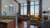 This two-floor, 2-bedroom, 2-bathroom loft-style residence blends industrial character with modern comfort. The main level impresses with soaring ceilings, exposed brick walls, and dramatic floor-to-ceiling factory-style windows that flood the space with natural light and offer expansive outdoor views. Rich, polished hardwood floors run throughout, anchoring the open-concept living and dining areas. The living room features a fireplace and ceiling fan, while the adjacent dining area provides an intimate space for everyday living. The well-appointed kitchen includes granite countertops, light wood cabinetry, stainless steel appliances, and a peninsula with bar seating — all topped by pendant lighting with a clear view to the loft above. Exposed ductwork and original structural beams add to the authentic industrial aesthetic. The upper loft level offers two bedrooms, each with warm hardwood floors and natural wood plank ceilings that lend a cozy, cabin-like contrast to the industrial main floor. One bedroom features a prominent structural column, adding architectural character. A flexible loft office nook with an exposed beam rounds out the upper level. Two full bathrooms — one featuring a tub/shower combo and granite vanity — complete this thoughtfully designed urban retreat.