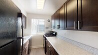 Unit 409 is a thoughtfully designed single-floor residence that combines modern finishes with a clean, functional layout. The kitchen serves as a standout feature, boasting rich dark cabinetry with sleek hardware, speckled stone countertops, a gas range, and a built-in skylight that floods the galley-style space with natural light. A window with horizontal blinds further brightens the kitchen and offers views of the surrounding exterior. Light wood-style flooring runs throughout the living and bedroom areas, creating a cohesive and contemporary aesthetic against the crisp white walls. The living area is generously proportioned and open, offering ample room for a variety of furniture arrangements. The bedrooms are well-sized, each featuring windows with natural light, and at least one includes a dedicated closet with a hanging rod for organized storage. The bathroom is finished in clean white with a full soaking tub and shower combination, complemented by a frosted window and built-in corner shelving for added practicality. Throughout the unit, consistent finishes, neutral tones, and wood-look flooring contribute to a bright, airy, and move-in-ready atmosphere.