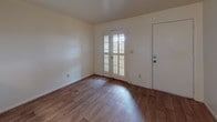 This single-story unit is thoughtfully arranged to maximize functionality across its connected living spaces. The layout flows from a welcoming entry area featuring rich wood-style flooring and a set of French doors fitted with louvered shutters, allowing natural light to filter in while maintaining privacy. A ceiling fan overhead adds to the comfortable, practical character of the space.

The galley-style kitchen is efficiently designed, with warm wood cabinetry lining both walls, dark granite-style countertops, a coil electric range, a full-size refrigerator, and a stainless steel sink. Upper and lower cabinets provide ample storage throughout. A pass-through window connects the kitchen to the main living area, enhancing the open feel between spaces.

The living and dining areas share the same wood-style flooring, creating a cohesive and spacious feel. White walls and neutral tones keep the atmosphere bright and clean throughout.

The bedroom is generously sized, featuring plush carpet flooring, a closet, and a window dressed with louvered shutters that allows natural light into the room. The bathroom includes a vanity with granite-style countertop, a sink, and a toilet, and is conveniently accessible from the central hallway that connects all rooms seamlessly.