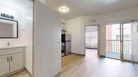 This thoughtfully designed one-bedroom, one-bathroom unit makes excellent use of its compact footprint across a single floor. Light wood-tone flooring runs continuously throughout the space, creating a cohesive and clean aesthetic. The open layout connects the kitchen and living areas, allowing natural light from the bedroom's large window to filter through the unit.

The kitchen is well-appointed with shaker-style grey cabinetry, a stainless steel refrigerator, gas range, and over-the-range microwave. A deep single-basin sink with a brushed nickel faucet and white tile backsplash complement the light countertops, while upper and lower cabinets provide ample storage.

The bedroom offers a comfortable and private retreat, benefiting from a large window that invites natural light. An adjacent walk-in closet features wire shelving and a clothing rod, offering organized storage space. The bathroom is clean and functional, equipped with a full soaking tub and shower combo outfitted with a handheld showerhead, a toilet, and a vanity with a white countertop. Brushed nickel fixtures and white walls maintain a crisp, contemporary feel throughout. An access door to an outdoor area adds additional ventilation and light to the overall space.