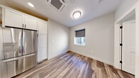 Located at 25 Lowell St in Manchester, NH, this efficiently designed one-bedroom, one-bathroom unit offers a thoughtfully laid-out single-floor plan with modern finishes throughout. The open-concept kitchen and living area serves as the heart of the space, featuring crisp white shaker cabinetry, warm-toned open wood shelving, and a suite of stainless steel appliances including a French door refrigerator, electric range, and built-in microwave. A sleek white quartz peninsula with an undermount sink and pendant lighting above provides both prep space and casual dining potential. Wood-look luxury vinyl plank flooring runs throughout the main living areas, adding warmth and visual continuity. The bedroom is a cozy, well-proportioned retreat with a large panel-style sliding closet and a window that allows natural light to filter in. A dedicated laundry area adds everyday convenience. The bathroom is finished with a white vanity, tile-look flooring, and matte black hardware accents that complement the clean, contemporary aesthetic found throughout the unit. Neutral gray and white tones, recessed and flush-mount lighting, and a ceiling-mounted HVAC unit complete this move-in ready space ideal for efficient urban living in downtown Manchester.