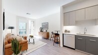 This thoughtfully designed 1-bedroom, 1-bathroom residence spans a single floor and offers a well-appointed open-concept layout that maximizes every square foot. Light-toned hardwood-style flooring flows throughout, tying together the living, dining, and kitchen areas seamlessly.

The kitchen is a standout feature, outfitted with two-tone cabinetry — light gray uppers and dark charcoal lowers — paired with white quartz countertops and a full suite of stainless steel appliances, including a range, over-the-range microwave, dishwasher, and refrigerator. A breakfast bar connects the kitchen to the open living and dining area, ideal for casual dining or entertaining.

The living room is bright and airy, benefiting from natural light streaming through large windows and a glass balcony door that opens to an outdoor space with exterior views. The bedroom offers a comfortable footprint with a large window, access to natural light, and dark hardwood flooring that adds warmth and contrast.

The bathroom features a dark charcoal floating vanity with a white undermount sink, a large mirror, and wood-look tile flooring. A well-organized walk-in closet with wire shelving systems provides ample storage. A hallway entry with recessed lighting completes this clean, modern, and functional residence.