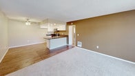 This single-floor residential unit offers a well-organized layout that balances functionality with comfort. The open-concept living and dining area transitions seamlessly between warm hardwood-style flooring and plush wall-to-wall carpeting, creating distinct zones within a connected space. A ceiling fan with integrated lighting serves the living area, which benefits from natural light streaming through large windows fitted with vertical blinds. The kitchen is a standout feature, showcasing white cabinetry, dark granite countertops, and a full suite of stainless steel appliances including a range, over-the-range microwave, and dishwasher. A peninsula counter provides additional prep space and separates the kitchen from the living area. The bedrooms are finished with soft carpeting and neutral warm-toned walls, with windows that bring in natural light. The bathroom is equipped with a dual-sink vanity featuring dark granite countertops, white cabinetry, framed mirrors, and a separate bathtub enclosure. Textured ceilings are consistent throughout the unit, and clean white baseboards provide a crisp finishing detail. Overall, the space presents a neutral, move-in ready aesthetic with practical finishes suited for everyday living.
