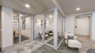 Located at 12387 San Jose Blvd in Jacksonville, Florida, this single-floor commercial space is thoughtfully designed to support both collaborative work and private meetings. The layout balances open seating areas with enclosed glass-walled rooms, creating a functional yet sophisticated environment throughout.

The glass-enclosed meeting pods are a defining architectural feature, constructed with sleek aluminum framing and full-height glass panels that maintain visual connectivity while providing acoustic separation. Each pod is furnished with comfortable seating, wall-mounted lighting, and artwork, lending a refined, professional feel. The pods open via full-glass doors, making them easily accessible and adaptable for various uses.

Open lounge areas complement the private pods, furnished with plush white and leather seating, accent tables, and decorative elements that keep the atmosphere welcoming. A built-in bench nook with pendant lighting and stone-top tulip tables offers an additional intimate gathering spot. Natural light filters in through large windows and glass doors leading to an exterior balcony, brightening the neutral-toned interiors. Textured carpet flooring with a muted, stone-like pattern grounds the space, while recessed lighting ensures consistent illumination throughout. The overall ambiance is modern, polished, and purposefully designed for productivity.