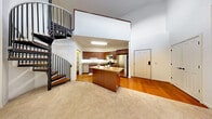 This two-story residence is defined by its dramatic architectural design, most notably the soaring double-height ceilings in the main living area that create an immediate sense of openness and volume. A sleek, wrought-iron spiral staircase serves as a visual centerpiece, connecting the two floors while adding a sculptural element to the space.

The kitchen is thoughtfully designed with rich warm-toned cabinetry, granite countertops, and a full suite of stainless steel appliances, including a refrigerator, range, microwave, and dishwasher. A central island provides additional prep and dining space. Hardwood flooring runs throughout the kitchen, transitioning to plush carpeting in the living areas.

The living room features a fireplace with a classic wood mantle and receives natural light through a large window. Access to an outdoor area is provided via a glass door. A dedicated laundry room with a full-size washer and dryer adds convenience.

The primary bathroom includes a dual-sink vanity with rich wood cabinetry, white countertops, and tile flooring. Bedrooms are carpeted and offer generous closet space, including a walk-in closet. The overall ambiance is warm, functional, and well-appointed throughout.
