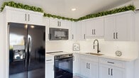 This thoughtfully designed single-floor unit offers a clean, modern aesthetic with a cohesive layout connecting all living areas. Light wood-look flooring runs throughout, complementing the bright white walls and recessed lighting that give the space an open, airy feel.

The living room is a welcoming focal point, anchored by a large picture window that frames outdoor street views and fills the room with natural light. A wall-mounted TV and a dedicated dining area with a compact table make the space both functional and comfortable.

The kitchen features crisp white shaker cabinetry adorned with matte black hardware, a white subway tile backsplash, and light quartz countertops. Stainless and black appliances — including a range, over-the-range microwave, and refrigerator — complete the space, while decorative greenery atop the cabinets adds a fresh, lively touch.

The bedroom is generously proportioned with two large windows on adjacent walls, flooding the room with natural light and offering open exterior views. A built-in double closet and a wall-mounted mini-split system provide practical comfort and storage.

The bathroom is finished in a clean, minimalist style with a wide white shaker vanity, matte black fixtures, an undermount sink, and an industrial-style vanity light. Every detail reflects a consistent modern design sensibility throughout this well-appointed space.