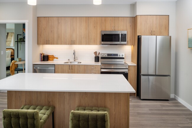 Kitchen with oak cabinetry, stainless steel appliances, granite countertops, and hard surface flooring - Avalon Redmond Campus