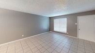 This single-floor space presents a practical and well-organized layout as revealed through its floorplan and interior views. The kitchen is equipped with white cabinetry extending to the ceiling for ample storage, gray speckled laminate countertops, a black electric range with overhead ventilation, a stainless steel double-basin sink, and a full-size refrigerator. A tiled backsplash and light tile flooring complete the functional cooking area.

The living and bedroom spaces feature neutral gray-toned walls, light ceramic tile flooring throughout, white baseboards, and textured ceilings. Each room benefits from natural light provided by windows fitted with horizontal blinds, giving the interior a bright and open feel.

Two bathrooms serve the unit. One features a tub-shower combination with full beige ceramic tile surround and a standard shower rod, while the second bathroom includes a white tub-shower unit with chrome fixtures and a matching shower rod. Both bathrooms maintain a clean, utilitarian design consistent with the rest of the space.

Overall, this single-story layout offers a cohesive and low-maintenance interior characterized by consistent tile flooring, neutral wall tones, and practical fixtures throughout each room.