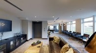 Located on Foster Street in Durham, NC, this single-floor communal space offers a thoughtfully designed open-plan layout that balances comfort and sophistication. The lounge area anchors the space with a rich, dark leather sofa accented by patterned throw pillows, set atop a large area rug over a wood-toned coffee table — creating a warm and inviting gathering spot. Recessed lighting runs throughout the smooth white ceiling, complemented by elegant globe pendant chandeliers that add a refined, modern touch.

Moving deeper into the space, a billiards table provides a focal point for recreation, while a row of sleek lounge chairs lines the perimeter near expansive floor-to-ceiling windows. These generous windows allow abundant natural light to pour in and offer views of the surrounding environment, enhancing the open, airy ambiance of the room. A dark cabinetry unit along one wall provides additional storage and display space.

The overall aesthetic blends contemporary design with warm, residential elements — neutral tones, layered textures, and curated furnishings — resulting in a versatile space well-suited for both relaxation and social interaction.