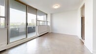 Located at 301 Dixon Rd in Toronto's west end, this well-appointed unit offers three bedrooms, two bathrooms, and a thoughtfully laid-out living space across a single floor. The open living room is a standout feature, showcasing classic parquet flooring, crisp white walls, and expansive floor-to-ceiling windows that bathe the room in natural light while framing views of the surrounding cityscape. A sliding glass door connects the living area to a balcony, further enhancing the sense of openness. The bedrooms continue the parquet flooring theme and are generously sized, with the primary bedroom offering a comfortable retreat. Each bedroom is equipped with sliding closet doors for practical storage. The two bathrooms are finished in a clean, modern style — one features subway-tiled walls surrounding a full soaker tub and shower combination, while the second includes a sleek white vanity with under-sink cabinetry and large-format tile flooring. The entry foyer provides a smooth transition into the unit, with a glimpse into the kitchen, which features stainless steel appliances. Throughout the unit, the bright, neutral palette and consistent finishes create a cohesive and functional living environment.