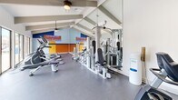 This fitness center at 2420 Riverfront Drive in Little Rock, Arkansas, is a thoughtfully designed workout facility that offers a comprehensive exercise environment across a single floor. The main gym area is characterized by striking vaulted ceilings with exposed beam detailing and ceiling fans, creating an open and airy atmosphere. Large floor-to-ceiling windows along one wall flood the space with abundant natural light and provide views of the outdoor pool area and surrounding grounds, enhancing the workout experience.

The facility is equipped with a wide array of modern exercise machines, including treadmills, ellipticals, and a variety of strength training equipment. A full wall of mirrors on one side expands the sense of space and allows users to monitor their form during workouts. A dumbbell rack and water station are also conveniently available. The floors are finished in durable rubber gym flooring, practical for high-activity use. A bold, colorful accent wall featuring the motivational branding "Let's Get Fit #BrightWaters" adds an energetic and inspiring touch to the space.

The facility also includes a clean, accessible restroom finished with tile flooring, dark wood cabinetry, and modern fixtures, ensuring convenience for all users. Overall, the fitness center presents a bright, functional, and motivating environment well-suited for a full range of workout routines.