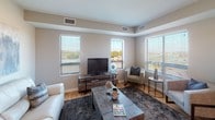 This single-floor residence offers a thoughtfully designed layout that balances functionality and comfort throughout its key living spaces. The kitchen serves as a standout feature, showcasing rich dark cabinetry extending to the ceiling, striking granite island countertops with a double undermount sink, and a full suite of stainless steel appliances. Pendant lighting illuminates the island, which provides additional seating via industrial-style barstools. Light hardwood-style flooring flows through the kitchen and connects to the living area, where multiple windows invite generous natural light and views of the surrounding landscape. A sliding door provides direct access to an outdoor balcony. The living room offers a spacious, open feel with neutral walls and room for comfortable furnishings. Two bedrooms feature plush carpeting and neutral tones; one includes a walk-in closet with built-in shelving and hanging rods. Both bathrooms are finished with dark wood vanities, white countertops, and tub-shower combinations with curtain rods. Light hardwood-style flooring continues in the bathrooms, complementing the consistent, cohesive design palette found throughout the entire residence.