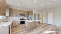 This contemporary two-story home in Shakopee, MN offers a well-designed layout spread across two floors. The main level features an open-concept living, dining, and kitchen area bathed in natural light from multiple windows. The kitchen stands out with warm-toned flat-front cabinetry, a subway tile backsplash, stainless steel appliances, and a central island with a crisp white countertop — ideal for both cooking and entertaining. Light wood-style flooring flows throughout the main level, complementing the clean, neutral palette and recessed lighting overhead.

The upper level houses all three bedrooms, three full bathrooms, and a dedicated laundry area with side-by-side washer and dryer. The generously sized primary bedroom features a tray ceiling, a ceiling fan, plush carpeting, and natural light from a well-placed window. The primary suite also benefits from impressive closet space, including a large walk-in closet with wire shelving on multiple walls. Additional bedrooms are well-proportioned and also feature carpeted floors. The bathrooms echo the home's modern aesthetic with wood-toned vanities, white countertops, and light wood-style tile flooring. An attached garage completes this thoughtfully appointed home.