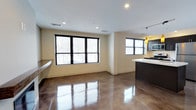 Unit 406 is a two-bedroom, two-bathroom single-level residence defined by a clean, contemporary aesthetic. The open-concept living and kitchen area serves as the heart of the space, anchored by striking polished concrete floors that reflect natural light and lend an industrial-modern character throughout. Large black-framed windows in the living area invite abundant natural light, creating a bright and airy atmosphere while offering views of the surrounding exterior. The seamless flow between the living space and kitchen makes the layout feel expansive and well-suited for both everyday living and entertaining. The kitchen features dark cabinetry paired with light countertops, creating a bold contrast that adds visual interest. A pendant light fixture above the kitchen area provides focused task lighting while contributing to the modern design palette. Recessed ceiling lighting is distributed throughout the open area, ensuring consistent illumination across the space. The neutral wall tones complement the flooring and cabinetry, maintaining a cohesive and understated color scheme. Overall, the unit presents a well-designed, modern living environment with durable finishes and thoughtful details.
