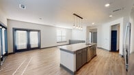 This single-floor unit offers a well-designed open-concept layout that seamlessly connects the kitchen and living area. The kitchen is a standout feature, centered around a large island with granite countertops, an undermount sink, and pendant lighting overhead. Grey shaker-style cabinetry pairs with a white subway tile backsplash and a full suite of stainless steel appliances, including a range, microwave, dishwasher, and refrigerator. A dedicated walk-in pantry with built-in shelving provides generous storage. Light-toned wood-style flooring flows throughout the main living areas, complementing the clean white walls and dark trim accents. The living space is bright and open, with multiple windows and French doors that invite natural light. The primary bedroom features plush carpeting, a ceiling fan, a walk-in closet with built-in shelving, and a private en-suite bathroom with granite counters, grey cabinetry, and a glass-enclosed shower. A second bedroom, also carpeted and ceiling fan-equipped, is served by a full bathroom featuring a double vanity with granite countertops and a shower-tub combination. The overall aesthetic is contemporary and cohesive, with consistent finishes tying each space together.