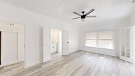 Located at 511 S Serrano Ave in the heart of Los Angeles, this 1-bedroom, 1-bathroom unit offers a clean, modern aesthetic throughout its efficiently designed single-floor layout. The main living area is bathed in natural light from large windows fitted with blinds, and features light wood-look laminate flooring and a sleek black ceiling fan that carries throughout the space. French-style doors connect the living area to the spacious bedroom, which is generously sized and includes two closets for ample storage, along with continued access to the bathroom area via a connecting hallway. The kitchen is a standout feature, boasting white shaker cabinetry with matte black hardware, a marble-style quartz countertop, a deep double-basin sink with a matte black faucet, and white appliances including a range and refrigerator. Marble-look tile flooring completes the kitchen's crisp, contemporary look. The bathroom continues the clean white palette with marble-style tile flooring, a full bathtub/shower combination, and classic black tile accent trim. A dedicated hallway with an additional closet and vanity cabinetry adds practical functionality. The overall ambiance is bright, minimalist, and move-in ready.