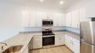This single-floor residence in Charlotte, NC, offers a clean, modern design throughout. The kitchen is a standout feature, equipped with crisp white cabinetry, granite-style countertops, stainless steel appliances including a refrigerator, range, and over-the-range microwave, and light wood-style flooring. A peninsula with a sink connects the kitchen to the open living area, which is brightened by recessed lighting and shares the same wood-style flooring for a cohesive look.

The bedrooms feature ceiling fans with light fixtures and neutral flooring — one with light hardwood-style planks and another with plush carpeting. A sliding glass door in one bedroom opens to an outdoor patio, providing direct access to natural light and exterior views.

The bathroom includes a granite-topped vanity with white cabinetry, a tub-shower combination, and hardwood-style flooring. Conveniently adjacent to the bathroom is an in-unit stacked washer and dryer, along with a walk-in closet with built-in shelving. Throughout the space, white walls, neutral finishes, and consistent design elements create a bright, well-organized living environment.