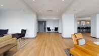 Located at 1184 Hank Aaron Dr in Atlanta, GA, this single-floor amenity space offers a generous, open-plan layout thoughtfully divided into multiple functional zones. Light hardwood flooring runs throughout, creating a warm and cohesive aesthetic that ties the various areas together seamlessly.

The space features a well-appointed kitchen and bar area with white cabinetry, a sleek white island with bar seating, and pendant lighting, positioned adjacent to a bright dining zone furnished with round tables and contemporary cream-upholstered chairs. Large windows along the perimeter flood this area with natural light and offer views of the surrounding Atlanta cityscape.

A relaxed lounge zone features comfortable sectional sofas, accent chairs, and area rugs, with French doors opening onto an outdoor balcony — a standout feature that extends the living space outdoors. Colorful artwork and built-in wall niches add visual interest throughout.

A separate high-top bar seating area with dark wood tables and black chairs provides a more casual social setting, accented by globe wall sconces and art pieces. Toward the far end of the space, a quieter lounge nook with accent chairs offers a more intimate retreat. Structural columns are integrated throughout, adding architectural character while defining each zone without the use of full partition walls.
