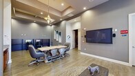 Located in Winter Garden, Florida, this community clubhouse offers a versatile and stylishly designed gathering space across a single floor. The layout encompasses distinct functional zones, each finished with consistent warm-toned luxury vinyl plank flooring and neutral gray walls that create a cohesive, modern aesthetic throughout.

The main lounge area welcomes visitors with large windows that flood the space with natural light, comfortable seating arrangements, and curated artwork displayed on the walls. A large flat-screen television is mounted prominently, complemented by plush accent chairs and area rugs that add warmth and texture.

A dedicated conference and meeting area features a substantial wood-topped table with rolling chairs, ideal for group gatherings or community events. A decorative geometric pendant light hangs above, accenting the tray ceiling detail that adds architectural interest and visual depth to the room.

The business center provides semi-private workstation cubicles equipped with desktop computers, ergonomic chairs, and ample desk space — a practical amenity for residents needing a quiet place to work or study.

The open clubhouse area offers expansive volume with high ceilings, large-format tile flooring, statement pendant lighting, and views to an outdoor area, creating an airy and inviting atmosphere. Together, these spaces form a functional and attractively appointed community hub.