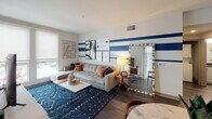 Located on West Pico Boulevard in Los Angeles, this contemporary single-floor residence showcases a thoughtfully designed open layout that maximizes both functionality and style. The kitchen is a standout feature, equipped with stainless steel appliances including a gas range, microwave, and a large French-door refrigerator. White cabinetry pairs elegantly with a sleek gray quartz countertop that extends into a breakfast bar, while open wooden shelving adds a modern, industrial touch. Recessed lighting throughout keeps the space bright and inviting.

The living area makes a bold visual statement with a striking blue and white striped accent wall, complemented by rich hardwood-style flooring. A generous sectional sofa, layered blue area rug, and curated décor create a comfortable yet stylish gathering space, with natural light flowing in through large windows.

The bedroom offers a calm retreat with soft neutral tones, roller shades, and a large window with street views, providing a peaceful and airy atmosphere. The bathroom is clean and modern, featuring a full tub and shower combo with white tile surround, a dark quartz vanity with an undermount sink, and wood-toned flooring that ties the space together cohesively.