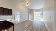Located at 925 NW 11th Ave in Portland's vibrant Pearl District-adjacent neighborhood, this single-floor unit showcases a thoughtfully designed open layout with notable architectural details throughout. The living area immediately impresses with its dramatically high ceilings and a distinctive curved bay window that floods the space with natural light and offers views of the surrounding streetscape and greenery. Light wood-style flooring runs continuously throughout, creating a cohesive, airy feel across all rooms.

The kitchen is well-appointed with rich dark-stained cabinetry, a classic white subway tile backsplash, stainless steel appliances including a refrigerator, range, and over-the-range microwave, and a quartz-topped peninsula with an undermount sink — an ideal setup for both everyday cooking and entertaining. The open connection between the kitchen and living area enhances the sense of spaciousness.

The bedroom areas feature soaring walls with large windows, a walk-in closet, and access to the hallway connecting to the bathrooms. The bathrooms are finished with wood-style flooring, a dark-stained vanity, and a full tub/shower combination with brushed nickel fixtures. A ceiling fan in the main living area and a wall-mounted AC unit add practical comfort to this bright, modern space.