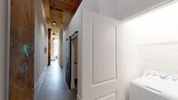 This single-floor unit in South Carolina masterfully combines industrial-loft heritage with contemporary design. The layout unfolds along a long corridor with polished concrete floors and soaring ceilings accented by exposed wooden beams and pendant lighting. A black sliding barn door adds a distinctive architectural detail, while original brick columns reinforce the building's historic character.

The kitchen is well-appointed with white shaker cabinetry, granite countertops, a herringbone-pattern tile backsplash, black hardware, and a full suite of stainless steel appliances including a gas range, dishwasher, and side-by-side refrigerator. A kitchen island provides additional prep and counter space.

The living area benefits from tall ceilings, exposed brick walls, and large windows that draw in natural light. The bedroom features dramatically high ceilings, polished concrete floors, and a dedicated closet. Two bathrooms serve the unit: one with a subway-tiled walk-in shower with black-framed glass door, and another with a soaking tub and shower combination. Consistent use of black fixtures, granite surfaces, and concrete flooring throughout ties the aesthetic together cohesively.
