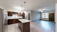 This single-floor residence is designed with an open-concept layout that seamlessly connects the kitchen and living areas, creating a spacious and functional flow. The kitchen is a standout feature, equipped with rich dark-walnut cabinetry, a built-in wine rack, subway tile backsplash, stainless steel appliances including a refrigerator with ice maker, range, microwave, and dishwasher. A large center island with a granite countertop provides additional prep space and casual seating. Pendant lights and a track light fixture illuminate the kitchen, while light wood-tone luxury vinyl plank flooring extends throughout the main living areas.

The living room offers a generous, open feel with neutral gray accent walls, a ceiling fan, and windows fitted with blinds that allow natural light to filter in. Two bedrooms feature plush carpeting, ceiling fans, and windows overlooking the exterior. Both bathrooms are clean and functional, each outfitted with a soaking tub and shower combination, chrome fixtures, and hard-surface flooring. The overall aesthetic is contemporary and cohesive, with a neutral palette and quality finishes throughout.