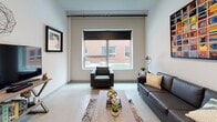 This well-appointed single-floor unit offers a thoughtfully designed layout that balances comfort and functionality. The living area serves as the heart of the space, featuring light-toned tile flooring, a large picture window with a roller shade that frames views of the surrounding brick exterior, and generous wall space showcasing framed artwork and decorative accents. The room flows naturally into the kitchen and dining area.

The kitchen is a standout feature, equipped with rich dark-espresso cabinetry, granite countertops, and a full suite of stainless steel appliances including a refrigerator, range, and over-the-range microwave. A peninsula with a granite overhang provides a casual dining spot with bar stool seating, making it an ideal space for both meal preparation and entertaining.

The unit includes two bedrooms, both finished with plush wall-to-wall carpeting and windows with roller shades that bring in natural light. The rooms offer clean, neutral walls well-suited for personalization.

The bathroom presents wood-look vinyl flooring, neutral tones, and a neatly appointed water closet area. Throughout the unit, the design aesthetic is consistently modern and understated, with clean lines, neutral color palettes, and practical finishes that create a cohesive and inviting living environment.