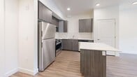 Located at 8283 S Main Street in Midvale, Utah, this well-designed one-bedroom, one-bathroom unit offers a thoughtfully laid-out floor plan with modern finishes throughout. The open-concept kitchen and living area serves as the heart of the home, showcasing dark wood-grain cabinetry, a classic white subway tile backsplash, crisp white quartz countertops, and a full suite of stainless steel appliances including a refrigerator, gas range, microwave, and dishwasher. A central kitchen island provides additional prep and dining space. Wood-look plank flooring flows seamlessly throughout the unit, complementing the clean, neutral color palette. The living area is bright and open, with access to a private balcony through sliding glass doors flanked by a window, allowing natural light to fill the space. The bedroom offers a comfortable footprint with a window overlooking greenery, recessed lighting, and easy access to the three closets spread throughout the unit, providing ample storage. The bathroom features a full tub-shower combo with built-in shelving, a vanity, and a clean, all-white finish. Recessed lighting and crisp white walls contribute to the modern, move-in-ready ambiance of this Midvale residence.