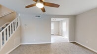 This two-bedroom, one-bathroom two-story home in Dundalk, Maryland offers a well-organized layout spread across two floors. The main level features a carpeted living room with a ceiling fan and open sightlines into the entry area, which benefits from natural light through front-facing windows. An adjacent dining room connects the living space to the kitchen, which has been updated with crisp white shaker cabinets, marble-style countertops, light wood-tone flooring, and stainless steel appliances including a gas range and refrigerator. A staircase with a white banister leads to the upper level, which houses both bedrooms, the full bathroom, and a hallway. The spacious primary bedroom features plush carpet, a ceiling fan, and a dedicated closet. The second bedroom offers dual windows that fill the room with natural light and is also carpeted with a ceiling fan overhead. The full bathroom is clean and bright, finished with light wood-tone flooring, a white vanity, a tub-shower combination, and gold-accented fixtures. Throughout the home, neutral gray walls and white trim create a cohesive, move-in-ready aesthetic. Four closets provide generous storage, and a utility room completes the home's functional layout.