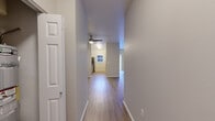 Located at 11028 E Portland Ave in Tacoma, WA, this single-story residence offers a clean, modern aesthetic throughout its thoughtfully designed layout. A central hallway with wood-look laminate flooring connects the living areas, drawing the eye toward the naturally lit kitchen and living space beyond. A ceiling fan overhead adds both function and a finishing touch to the open-feeling common areas.

The kitchen is equipped with a stainless steel refrigerator and benefits from a window that brings in natural light and views of the surrounding landscape. Adjacent rooms feature a mix of wood-look laminate and plush carpeting, providing both durability and comfort depending on the space's purpose. Several rooms offer views of the lush, tree-lined surroundings through large windows fitted with blinds, enhancing the connection to the natural environment outside.

Two bathrooms are present in the unit, each featuring a soaking tub and shower combination with built-in shelving, a curved shower rod, and wood-look flooring—offering a clean, functional design. The neutral color palette of warm whites and soft beiges carried throughout creates a cohesive and welcoming atmosphere well-suited to a variety of furnishing styles.