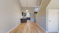 This two-story, 3-bedroom, 2-bathroom home offers a thoughtfully designed layout spread across two floors. The main level features an open-concept living, dining, and kitchen area distinguished by soaring vaulted ceilings and light wood-look flooring throughout. The kitchen is a standout, showcasing dark espresso shaker-style cabinetry, granite countertops, stainless steel appliances, recessed lighting, and a peninsula with bar seating — all illuminated by stylish pendant lights. The living and dining areas flow seamlessly from the kitchen, enhanced by the dramatic ceiling height that fills the space with an airy, open feel. The main floor also includes an attached garage with an automatic opener and an electrical panel, as well as utility areas and hallways for added convenience. Upstairs, the three bedrooms are finished with plush carpeting and offer generous closet space, including walk-in options. The primary bedroom is notably spacious and connects to a bathroom with a dedicated walk-in shower. Additional bedrooms feature ceiling fans and ample natural light. The second bathroom is clean and functional. Outside, a sturdy wood privacy fence with decorative lattice detailing encloses the property, providing a secure and private outdoor environment.