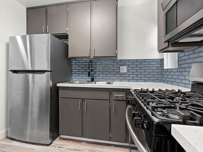 Blue tiled kitchen with stainless steel fridge, oven, and microwave. - Olive View Gardens