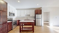 This well-appointed two-bedroom, two-bathroom unit at 201 Eldorado Dr in Jordan, MN offers a thoughtfully designed single-floor layout with generous living space. The open-concept kitchen and living room serves as the heart of the home, featuring warm light wood flooring, recessed lighting, and large sliding glass doors that lead to a private balcony with outdoor views. The kitchen is outfitted with a two-tone cabinetry design — rich espresso lower cabinets paired with crisp white uppers — complemented by a stylish tile backsplash, light countertops, stainless steel appliances including a range, microwave, and refrigerator, and a freestanding kitchen island for additional prep and storage space. The entryway provides a welcoming arrival with tall built-in cabinetry for convenient storage. Both bedrooms are bright and sun-filled, benefiting from natural light streaming through large windows. The primary bedroom includes a walk-in closet with wire shelving. The two bathrooms offer clean, modern finishes — one featuring a tub/shower combo and the other a walk-in shower. Additional highlights include a dedicated laundry area, a utility room, and three closets throughout, ensuring ample storage. The consistent light wood flooring and neutral palette create a cohesive, airy ambiance throughout the entire unit.