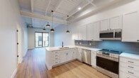 Located at 349 E Main Ave in Zeeland, MI, this thoughtfully designed one-bedroom, one-bathroom residence offers a compelling blend of industrial character and modern finishes throughout its single-floor layout. The open-concept kitchen and living area serves as the heart of the space, anchored by a sleek white peninsula with an undermount sink, crisp white shaker cabinetry, and a blue-grey subway tile backsplash. Stainless steel appliances — including a side-by-side refrigerator, electric range, dishwasher, and built-in microwave — provide a fully equipped culinary experience. Striking exposed wood-beam ceilings soar overhead, accented by pendant lighting and visible structural elements that lend an industrial-loft aesthetic. Warm-toned hardwood-style flooring flows throughout. Large black-framed sliding glass doors and windows flood the living area with natural light and offer views of the surrounding streetscape. The generously sized bedroom features a black-framed window with urban views and direct access to a well-organized walk-in closet with built-in shelving and hanging rods. A charming reclaimed wood barn door adds a rustic touch near the pantry. The full bathroom is finished with marble-look tile flooring, white subway tile surround, a tub/shower combo, and matte black fixtures throughout.
