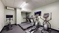 Located at 601 N Broad St in Philadelphia, PA, this fitness center offers a well-equipped exercise facility across a single floor. The space is thoughtfully organized to accommodate a variety of workout routines, with distinct zones for cardio, strength training, and functional fitness. The cardio area features multiple treadmills and elliptical machines, each equipped with individual digital consoles, complemented by a wall-mounted flat-screen TV for entertainment during workouts. The strength training section includes a full rack of dumbbells in varying weights alongside several selectorized resistance machines, providing options for both isolated and compound exercises. A dedicated functional fitness zone features stability balls, medicine balls, and a stretching board, anchored by a large floor-to-ceiling mirror that amplifies the sense of space. Throughout the facility, durable rubber-composite flooring provides comfort and safety underfoot, while a drop ceiling with recessed fluorescent lighting ensures consistent, bright illumination. Soft sage-green walls create a calm, focused atmosphere. A wall-mounted split AC unit maintains comfortable climate control. A sanitation station near the entrance promotes cleanliness. The layout is efficient and accessible, making this a comprehensive fitness amenity suited for a full range of exercise needs.