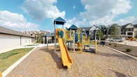 This residential community combines functional amenities with thoughtfully designed outdoor spaces. The architecture is characterized by multi-story brick buildings with warm tan and red tones, bay windows, pitched rooflines, and private balconies, lending a classic, traditional aesthetic throughout the property.

The outdoor pool area serves as a central gathering point, featuring a spacious brick-paver sundeck lined with blue lounge chairs ideal for relaxing. The pool is complemented by an adjacent patio furnished with umbrella-shaded tables and chairs, creating an inviting space for socializing. Manicured landscaping, including mature trees, trimmed shrubs, and well-maintained lawn areas, frames the pool deck and enhances the overall atmosphere.

A courtyard area provides additional outdoor living space, featuring brick-paver pathways, seating arrangements beneath large shade umbrellas, and lush greenery that adds privacy and a sense of tranquility between the buildings.

The community also includes a dedicated children's playground equipped with a multi-level play structure featuring a yellow slide, climbing elements, and yellow safety railings, all set atop a rubberized gravel surface. A covered gazebo with seating is positioned nearby, offering a shaded space for supervising caregivers. The playground is set within an open area, with the surrounding residential buildings and mature trees providing a comfortable, enclosed environment.