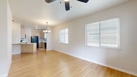 This single-floor residence offers a clean, contemporary design highlighted by light wood-tone flooring that runs consistently throughout the space. The open-concept living and dining area is generously proportioned, with vaulted ceilings that enhance the sense of volume. A ceiling fan with an integrated light fixture anchors the living area, while a pendant chandelier marks the dining zone. Two windows fitted with horizontal blinds allow natural light to fill the space and provide views of the surrounding exterior.

The kitchen is efficiently laid out in a galley-style configuration, featuring light wood cabinetry with modern hardware, white countertops, and black appliances including a refrigerator, range, and over-the-range microwave. A stainless steel sink sits beneath a window, adding additional natural light to the workspace.

The bedroom areas are calm and neutral, with the same light wood flooring and windows with blinds. One room includes a walk-in closet with built-in shelving and hanging rods, offering practical storage. The bathroom features a single-sink vanity with a wood-toned cabinet, a mirror, and a shower/tub combination. Decorative patterned tile flooring adds a subtle design accent to the otherwise neutral palette.