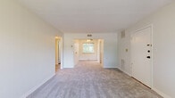 Located at 22437 Lorain Rd in Fairview Park, Ohio, this single-floor, 2-bedroom, 1-bathroom unit offers a straightforward and functional layout across a compact footprint. The living room serves as the central gathering space, finished with neutral carpet and clean white walls. A front entry door opens directly into this area, which flows into a secondary room equipped with a ceiling fan — visible through an open doorway — and a window framing views of surrounding greenery.

Both bedrooms are carpeted and finished with neutral tones. The primary bedroom features two windows that allow natural light to filter in and provide pleasant outdoor views of mature trees. The second bedroom similarly benefits from window views and a ceiling fan overhead. A hallway connects the bedrooms to the shared bathroom, which includes a tub-shower combination with white tile surround, wood-look flooring, and a small window.

The kitchen is a distinct space with wood-look flooring, dark lower cabinetry contrasted by white upper cabinets, a stainless steel sink with a modern faucet, light countertops, and a window overlooking greenery. The unit's consistent neutral palette and carpeted living areas contribute to a clean, move-in ready aesthetic throughout.