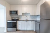 Located at 1200 Talwood Crt in Peterborough, Ontario, this well-designed 3-bedroom, 2-bathroom unit offers a comfortable and functional single-floor layout. The interior is finished with light-toned hardwood flooring throughout, crisp white walls, and clean baseboard detailing that give the space a bright, modern aesthetic.

The spacious living room is bathed in natural light from a large sliding glass door that opens onto a private balcony, offering outdoor views of the surrounding neighbourhood. The kitchen is thoughtfully appointed with white shaker-style cabinetry, dark countertops, a subway tile backsplash, stainless steel appliances including a full-sized refrigerator and dishwasher, and a double sink — providing both style and practicality.

The three bedrooms are well-proportioned and filled with natural light, each featuring the same warm hardwood flooring. The primary bedroom offers a generous footprint with ample space for furnishings. Both bathrooms are finished in a clean, contemporary style — one featuring a white vanity with chrome fixtures and a backlit mirror, and the other showcasing a full tub surround clad in classic white subway tile. A dedicated closet and hallway complete the functional floor plan of this move-in-ready unit.