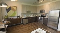 Located at 6750 E. Chenango Ave. in Denver, Colorado, this single-floor residence offers a thoughtfully designed living space with modern finishes and a clean, contemporary aesthetic. The kitchen serves as a standout feature, showcasing an L-shaped layout with rich dark lower cabinetry contrasted by light upper cabinets, creating a striking two-tone effect. A sage green subway tile backsplash adds a pop of color and texture, complementing the light stone countertops. Stainless steel appliances — including a range, microwave, and dishwasher — provide a sleek, polished look. A track lighting system overhead ensures the space is well-lit and functional. The kitchen opens to the living area, promoting an open-concept flow throughout the home. Rich, dark hardwood-style flooring runs throughout, anchoring the space with warmth and depth. The overall ambiance is modern and inviting, with a careful balance of contrast between light and dark tones, quality materials, and purposeful design choices that come together to create a stylish and practical living environment.