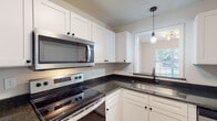 Located at 205 Partners Way in Fayetteville, NC, this single-floor residence offers a well-designed layout with thoughtfully updated interiors. The kitchen is a functional highlight, featuring white shaker-style cabinetry, dark granite countertops, stainless steel appliances including an electric range, built-in microwave, and dishwasher, along with a pendant light above the sink area and a window that brings in natural light. Light wood-style flooring runs throughout the main living areas, complementing the neutral wall tones. The bedrooms are comfortably sized, each equipped with a ceiling fan and windows fitted with blinds that allow for ample natural light and outdoor views. The primary bathroom stands out with a dual-sink vanity featuring slate-blue cabinetry, white countertops, and dark hardware, with a walk-in closet visible in the background. Additional bathrooms include tub/shower combinations with clean, simple surrounds. A dedicated laundry area accommodates a full-size side-by-side washer and dryer. The textured ceilings and consistent flooring tie the home together with a cohesive, move-in-ready aesthetic throughout every room.