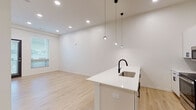 Located at 6530 Troost Ave in Kansas City, MO, this single-floor unit showcases a clean, modern design defined by bright white walls, light hardwood flooring, and recessed lighting throughout the main living areas. The open-concept layout seamlessly connects the kitchen and living space, creating a generous, airy feel enhanced by soaring ceilings.

The kitchen serves as a focal point of the space, anchored by a large white island with a quartz countertop, an undermount sink, and a matte black faucet. Pendant lights hang above the island, adding a stylish accent. White cabinetry lines the walls alongside a dark tile backsplash, and the kitchen is fully equipped with stainless steel appliances, including a French door refrigerator, range, and built-in microwave.

The living area extends naturally from the kitchen, offering an open, flexible space with natural light filtering in through blinds. Additional rooms feature the same light hardwood flooring, with at least one carpeted bedroom offering a softer underfoot feel and a window with outdoor views.

The bathroom maintains the unit's contemporary aesthetic, featuring a wide white vanity with quartz countertop, matte black hardware, an undermount sink, and a wall-mounted mirror with overhead lighting. Throughout, the space reflects a cohesive, minimalist sensibility with high-quality finishes.